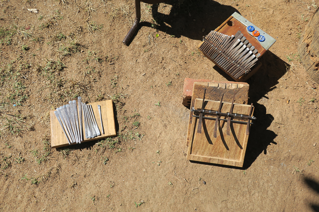 Mbira keys, a partly finished soundboard, and a completed instrument lie on the ground at Sekuru Chigamba's mbira workshop